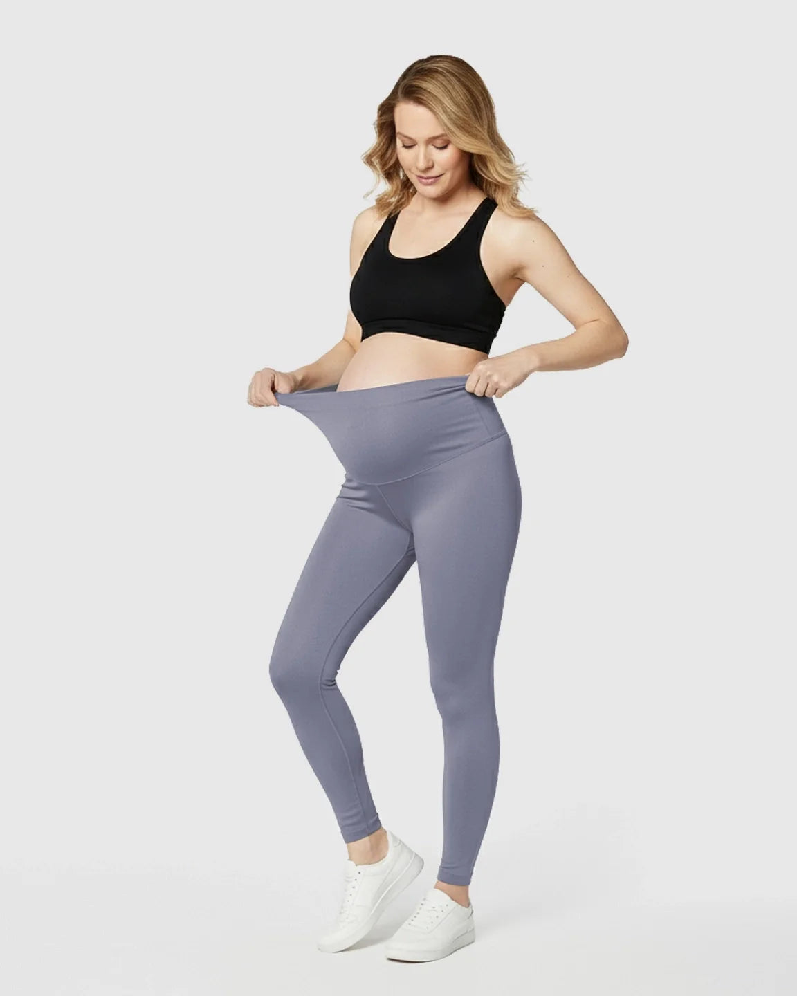 Pregnant woman in black sports bra pulling up soft, stretchy grey maternity midi leggings.