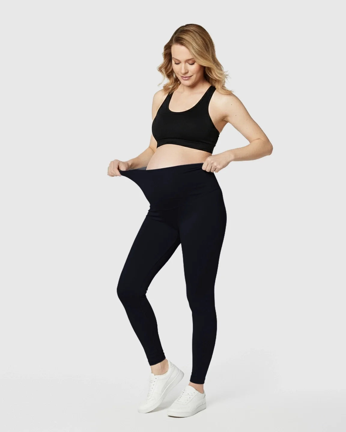 Pregnant woman in black maternity midi leggings with a seamless, C-friendly waistband and black bra.