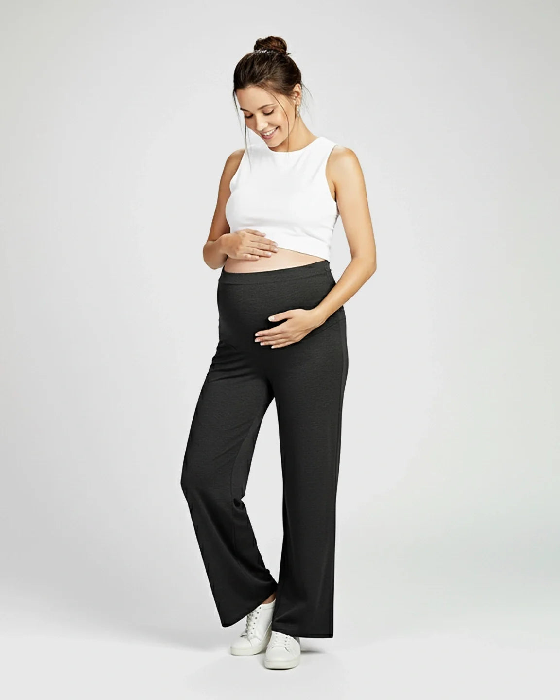Smiling pregnant woman in charcoal gray Comfort Fit Maternity Pants with elastic waist and white crop top.