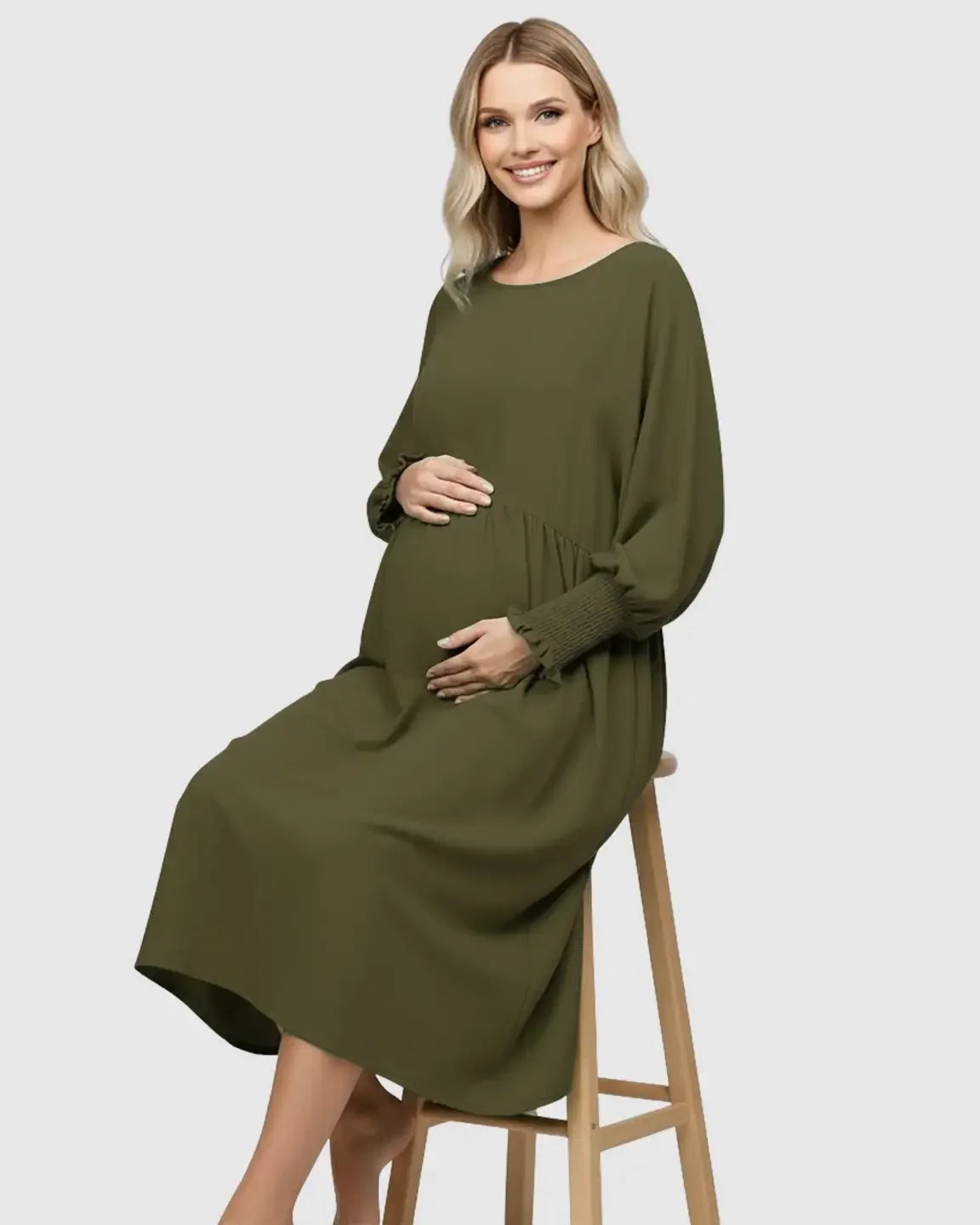 Smiling pregnant woman in a flowy olive green smocked sleeve casual dress with a round neckline.