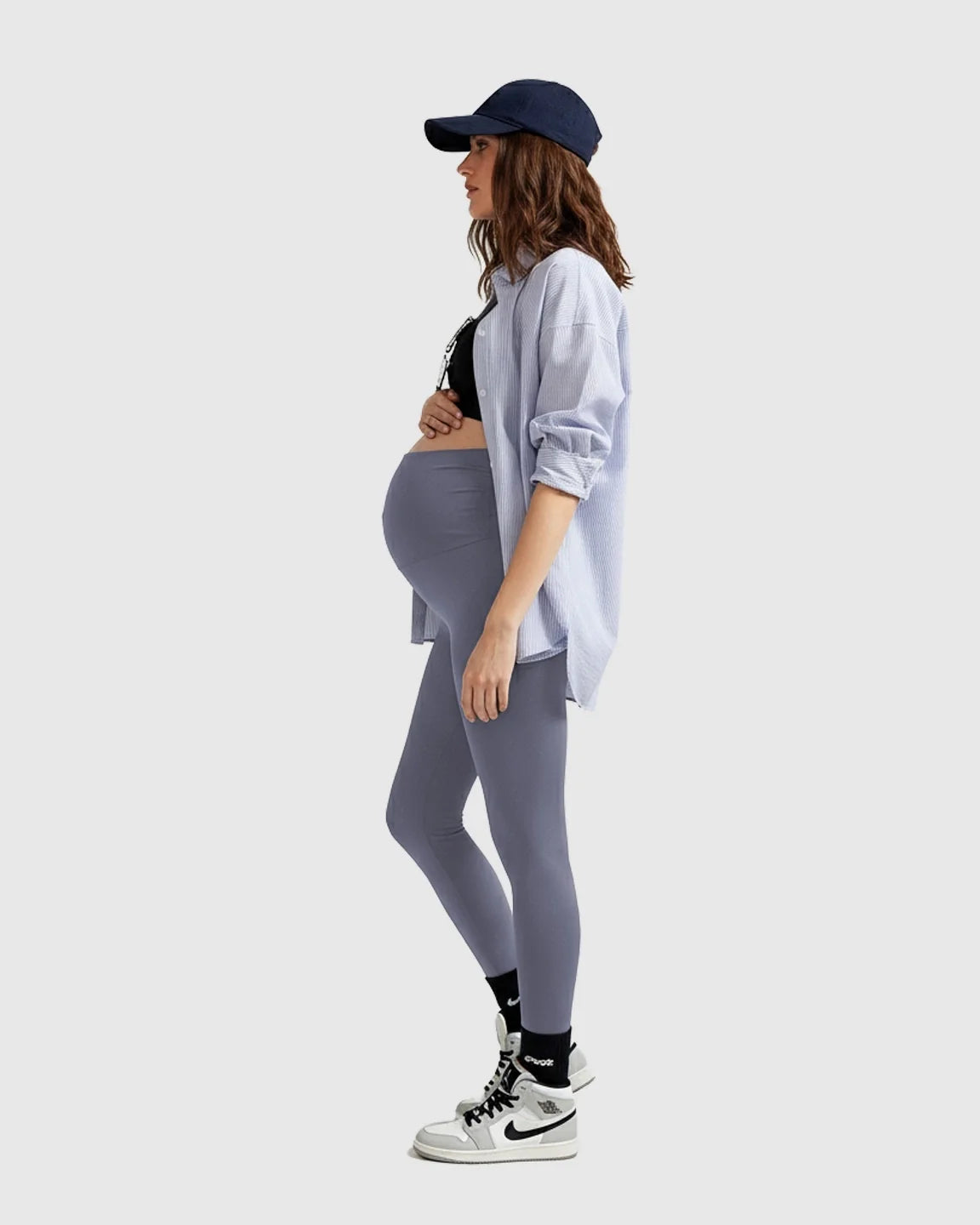 Pregnant woman in profile wearing slate gray Ultra-Soft Support Maternity Midi Leggings, a black bra, and a striped shirt.