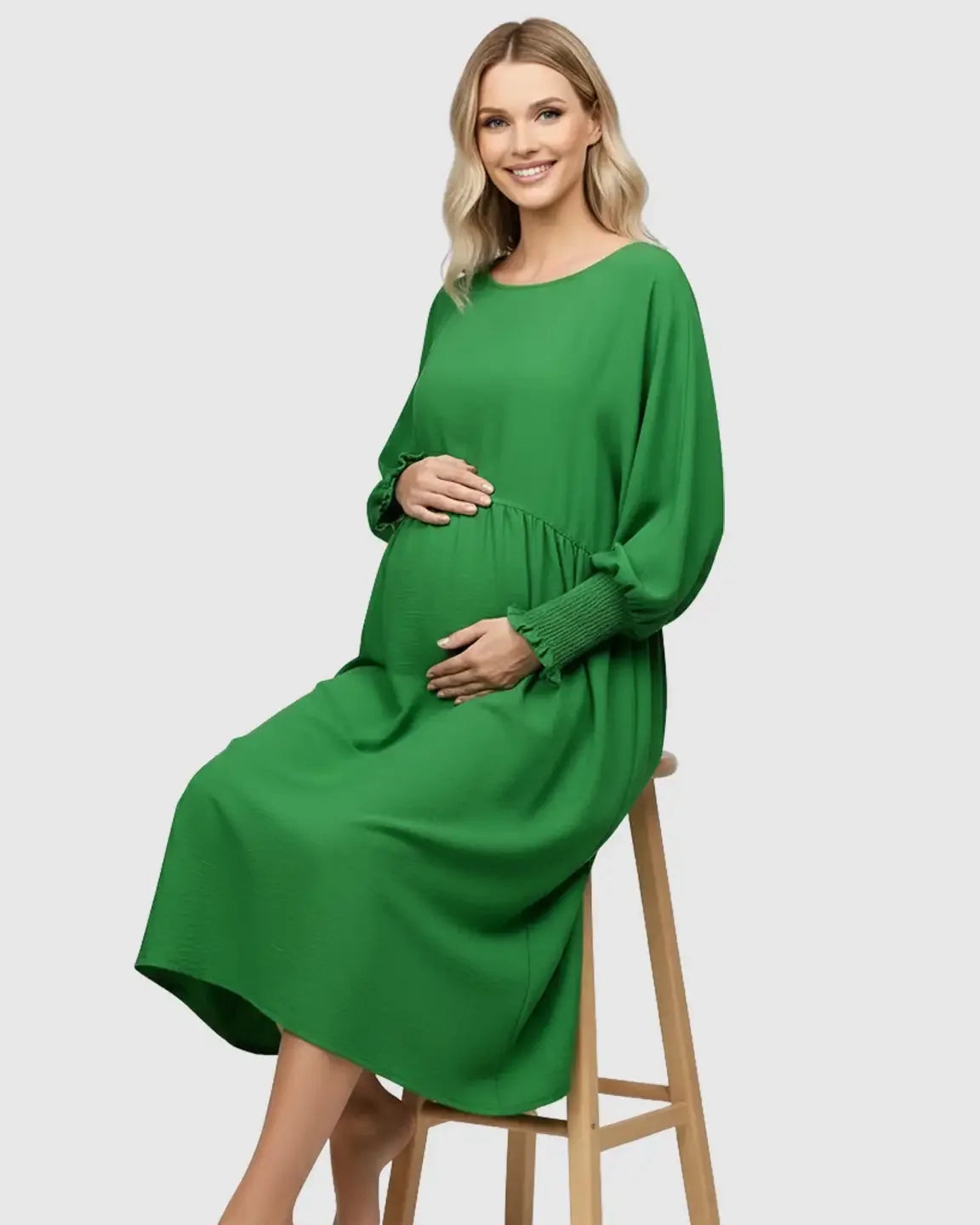 Smiling pregnant woman in a green flowy smocked sleeve casual dress with a round neckline.