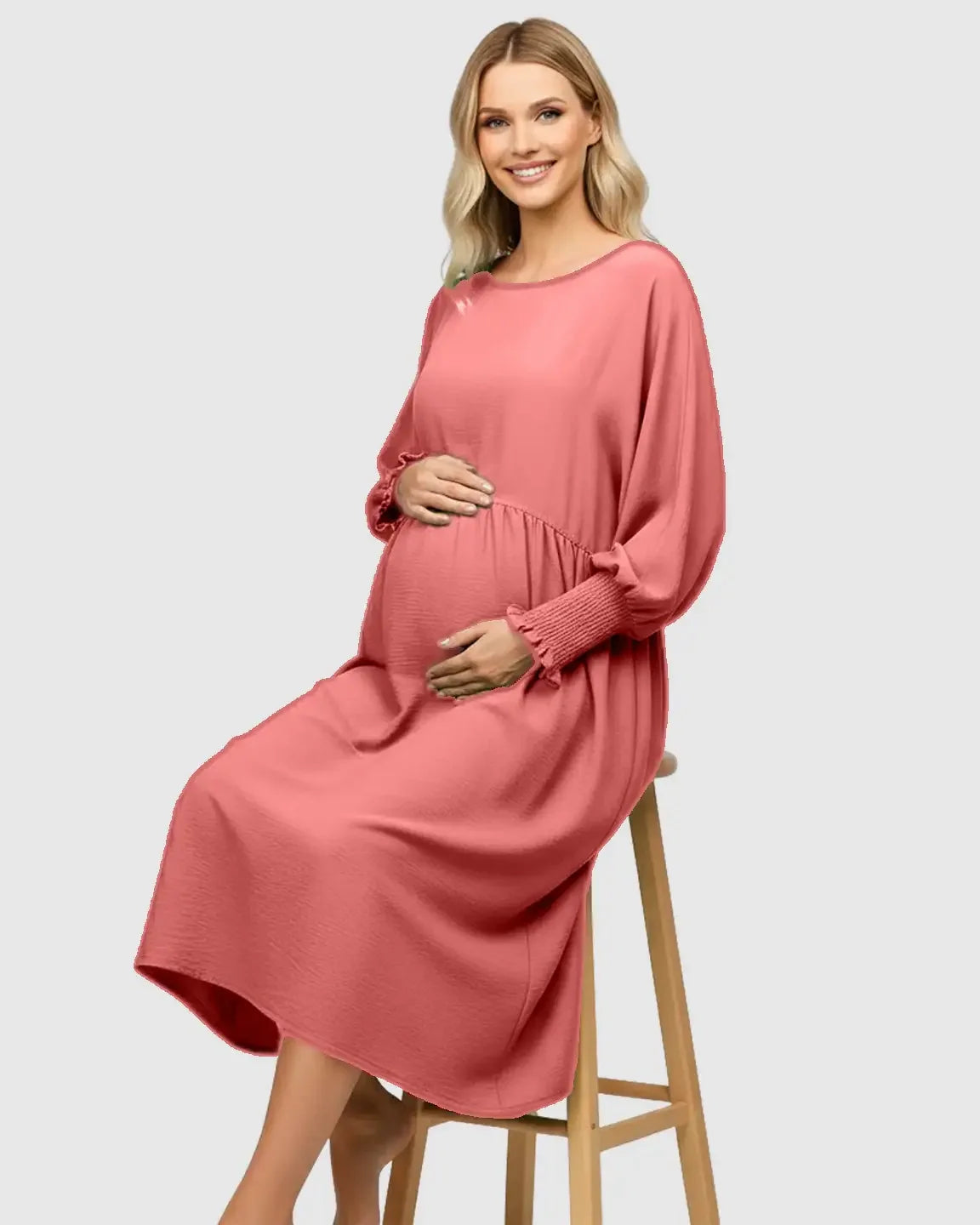 Smiling pregnant woman in a coral smocked-sleeve casual maternity dress, seated.