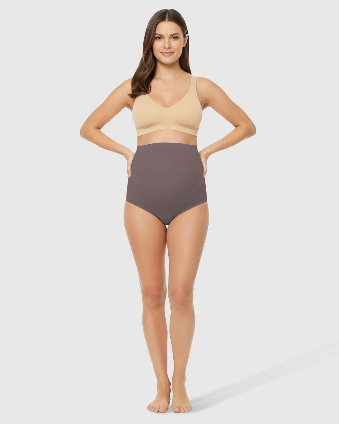 Woman in high-waist seamless belly-support maternity underwear in a dark gray color, paired with a beige bra.