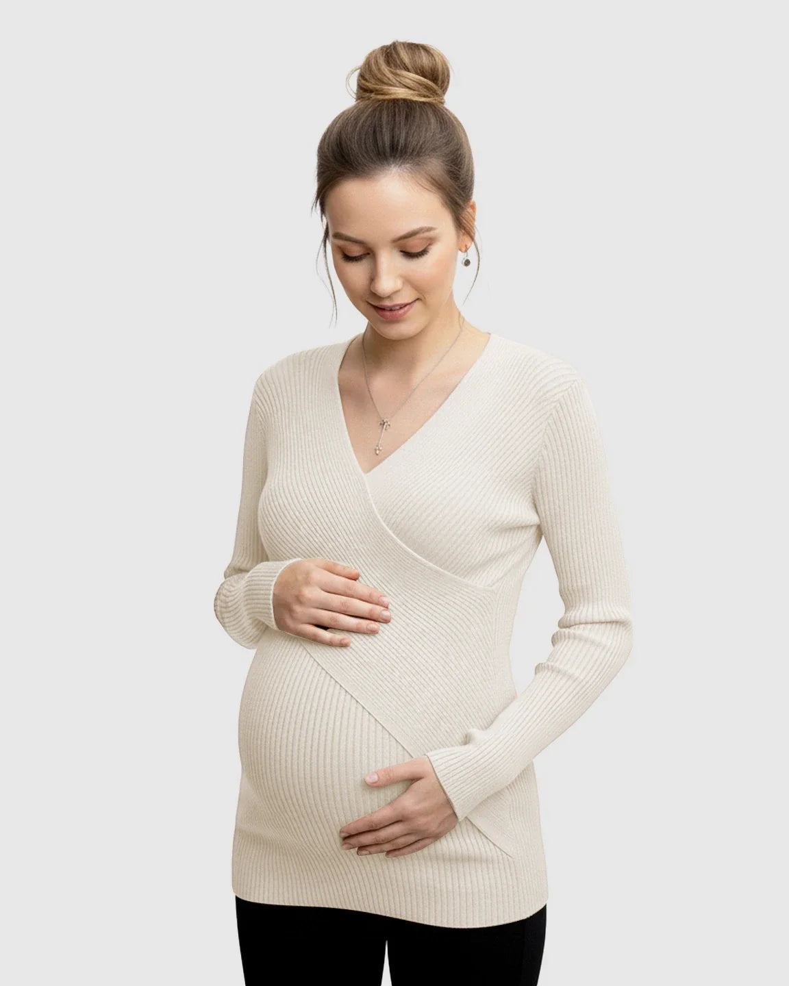 Pregnant woman in a cream faux-wrap ribbed maternity top, gently holding her bump.