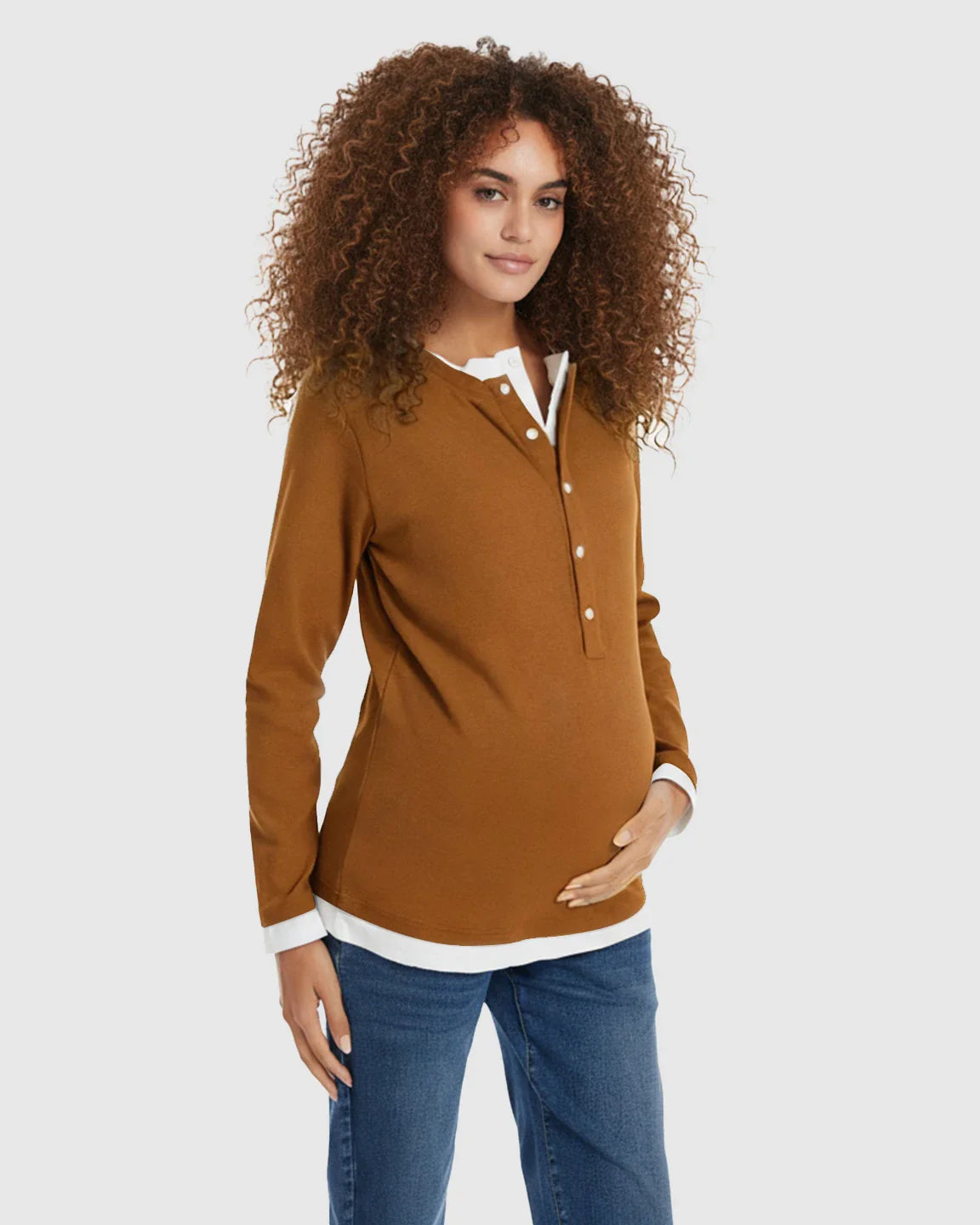 Pregnant woman in a brown long-sleeve henley maternity and nursing top with white trim and blue jeans.