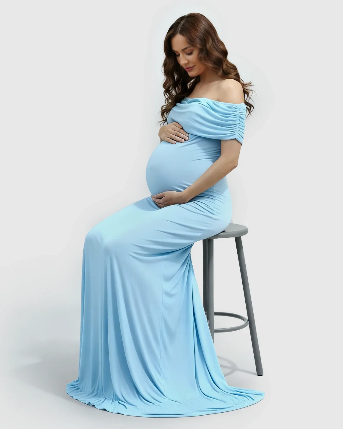 Pregnant woman in a light blue off-shoulder bodycon maternity mermaid gown, seated.