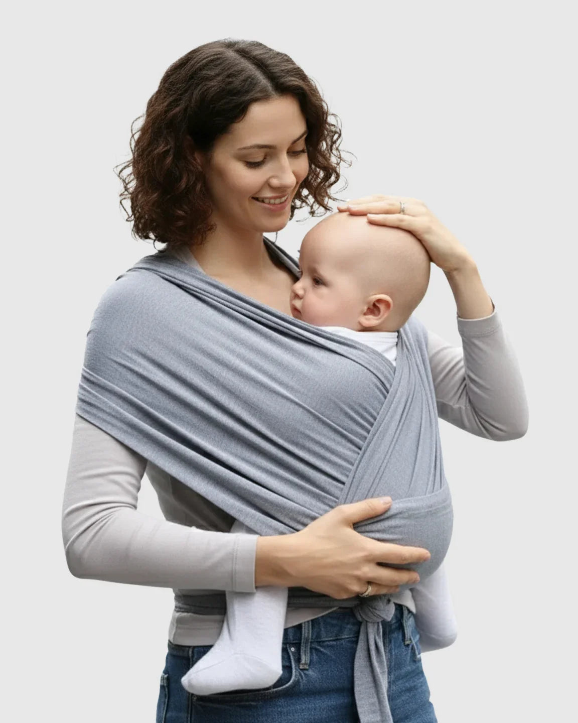 Woman smiling, holding a baby in a soft, light gray adjustable wrap-around baby carrier.