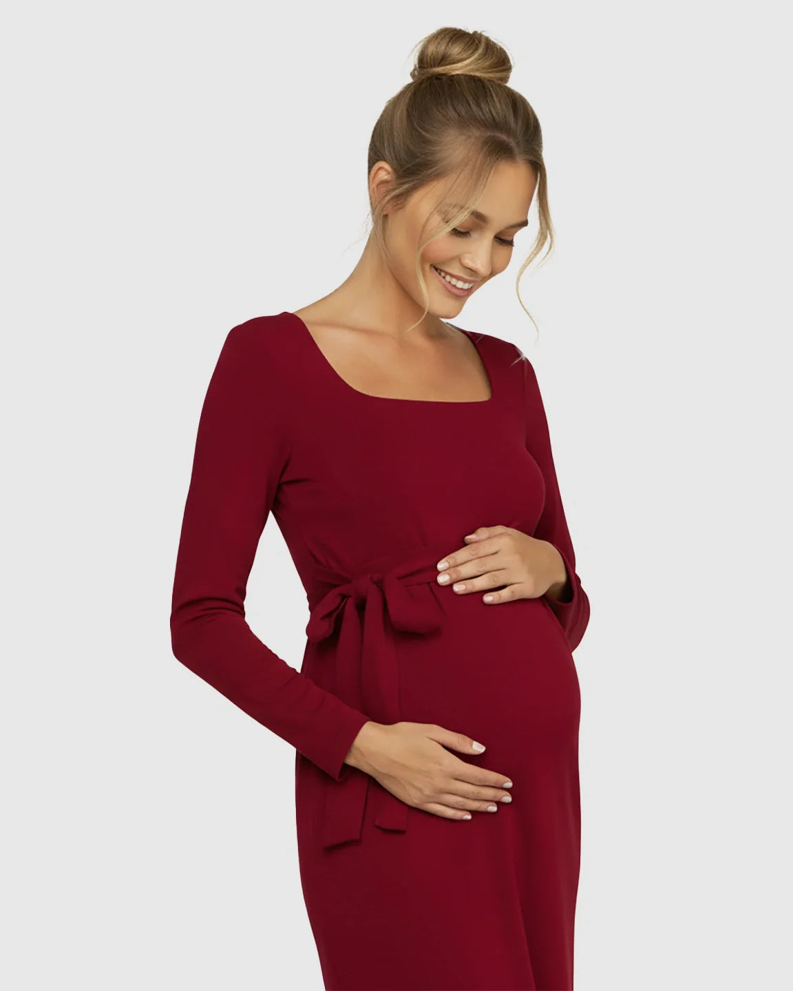Pregnant woman in a red square neck, long-sleeve bodycon maternity midi dress with an adjustable side-tie.