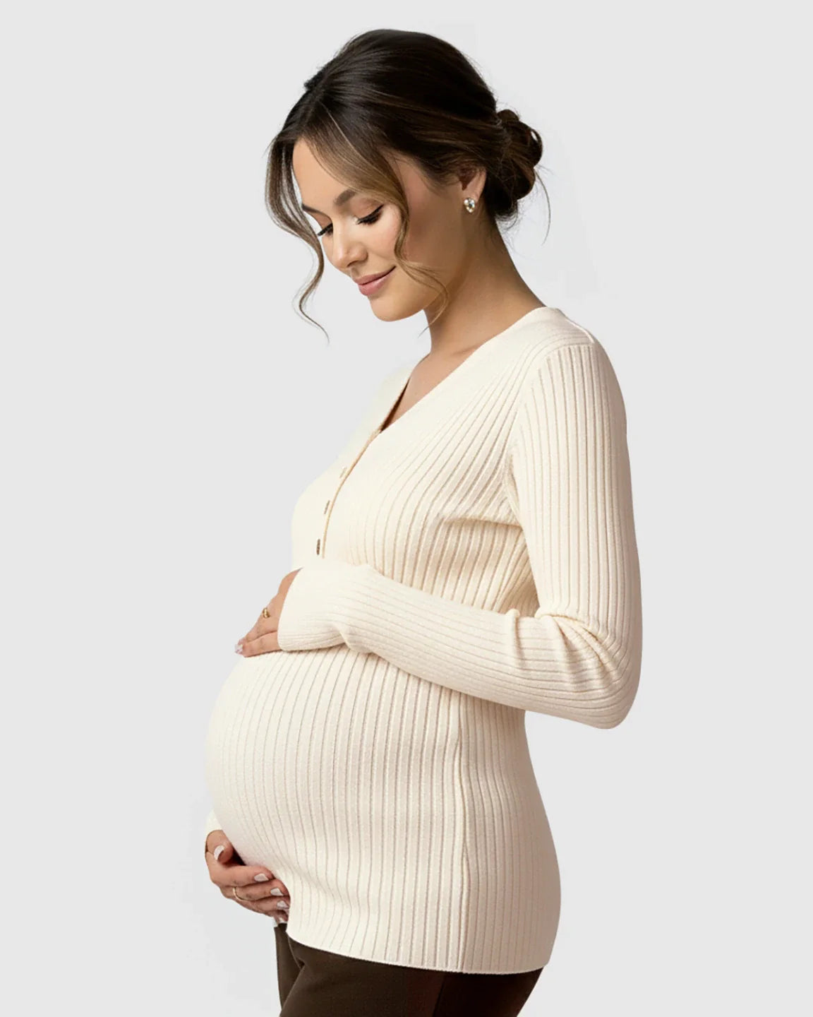 Pregnant woman in a cream ribbed V-neck maternity nursing sweater, gently holding her belly.