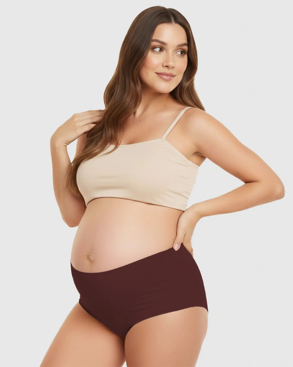 Smiling pregnant woman wearing a beige seamless maternity bra and high-waist maroon support underwear.