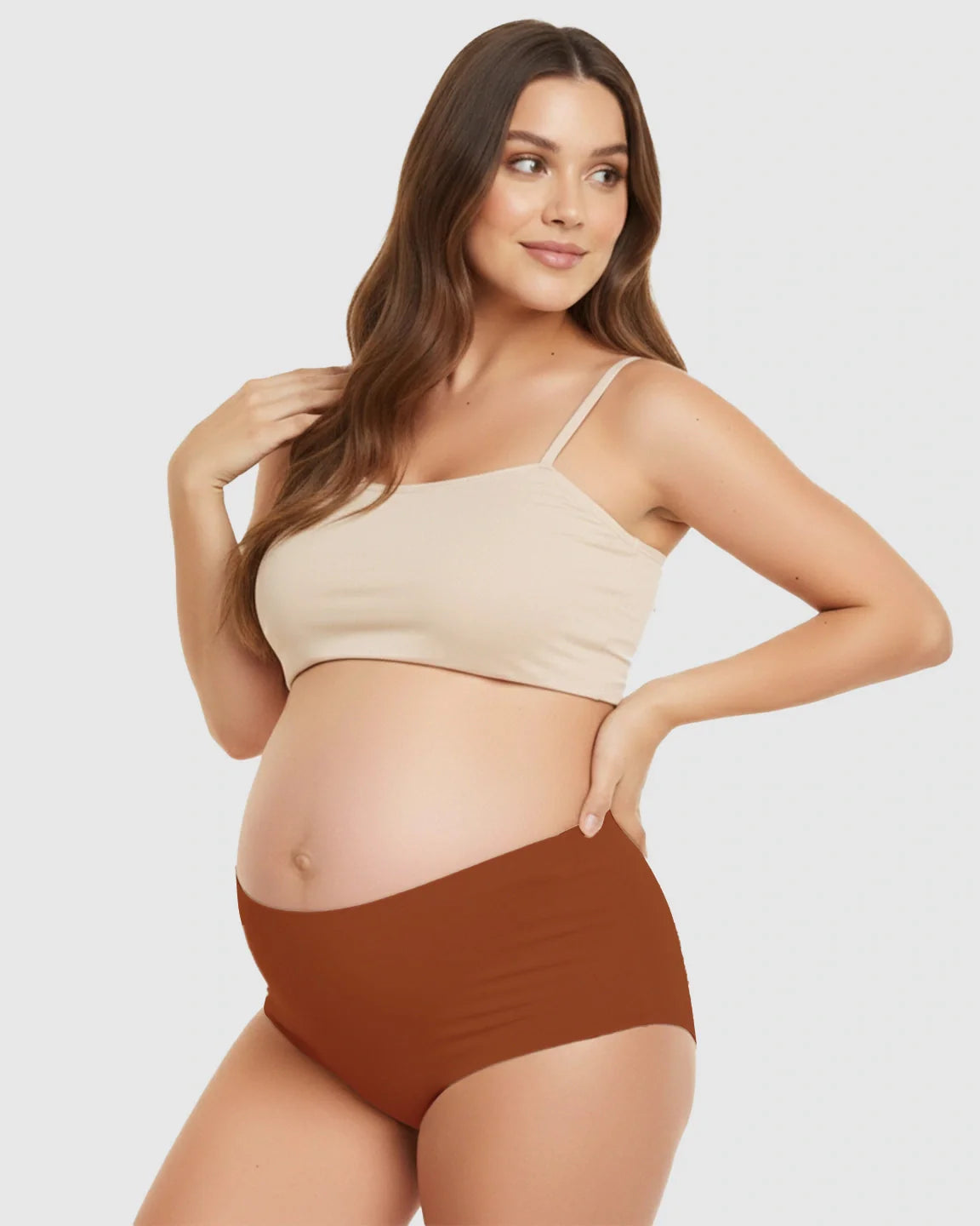 Pregnant model wearing seamless high-waist support maternity underwear in rust and a beige crop top.