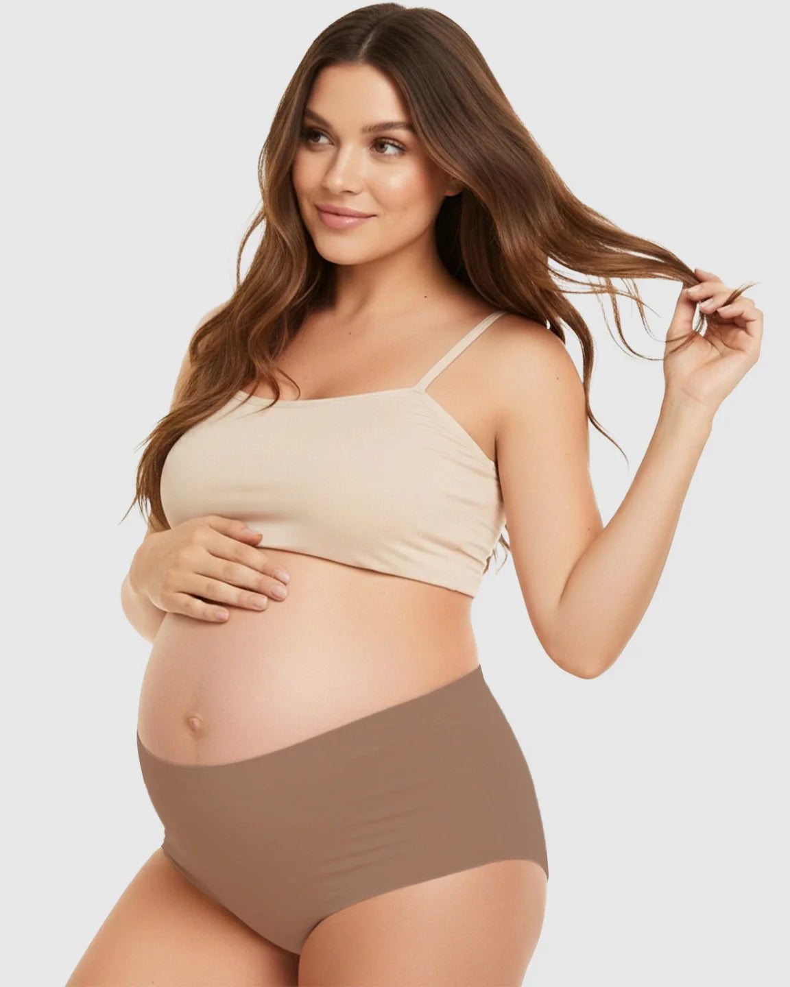 Pregnant woman in seamless high-waist support maternity underwear and a matching beige bra, gently holding her belly.