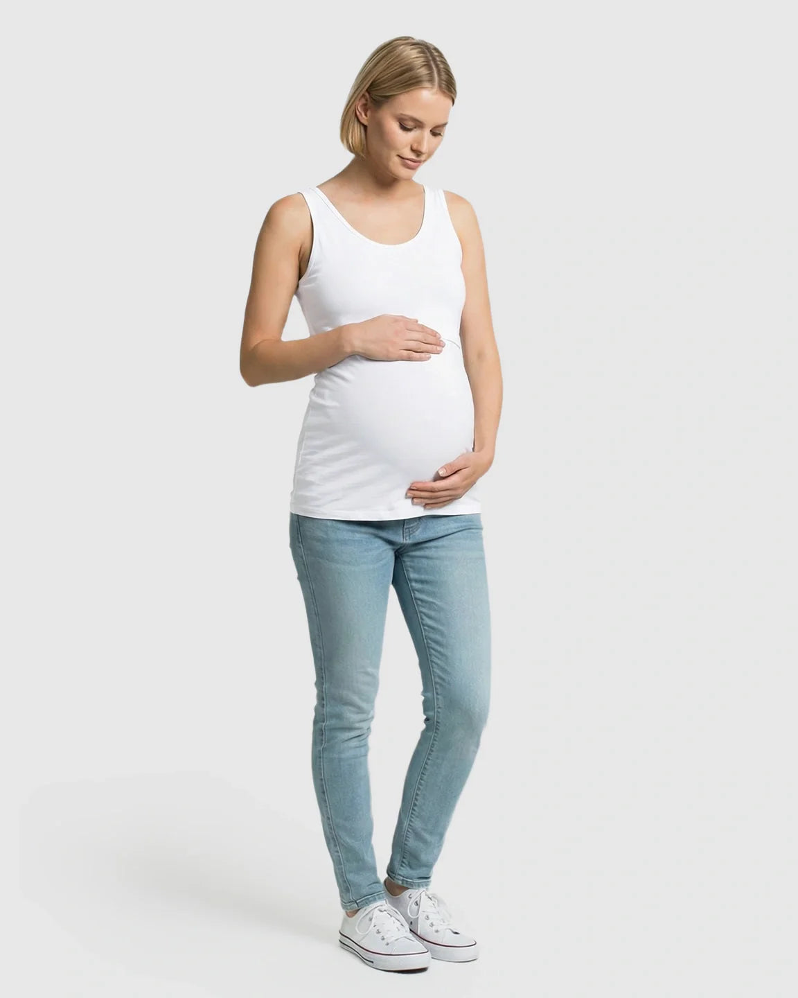 Pregnant woman in a white stretch nursing-access maternity tank top and light wash jeans.