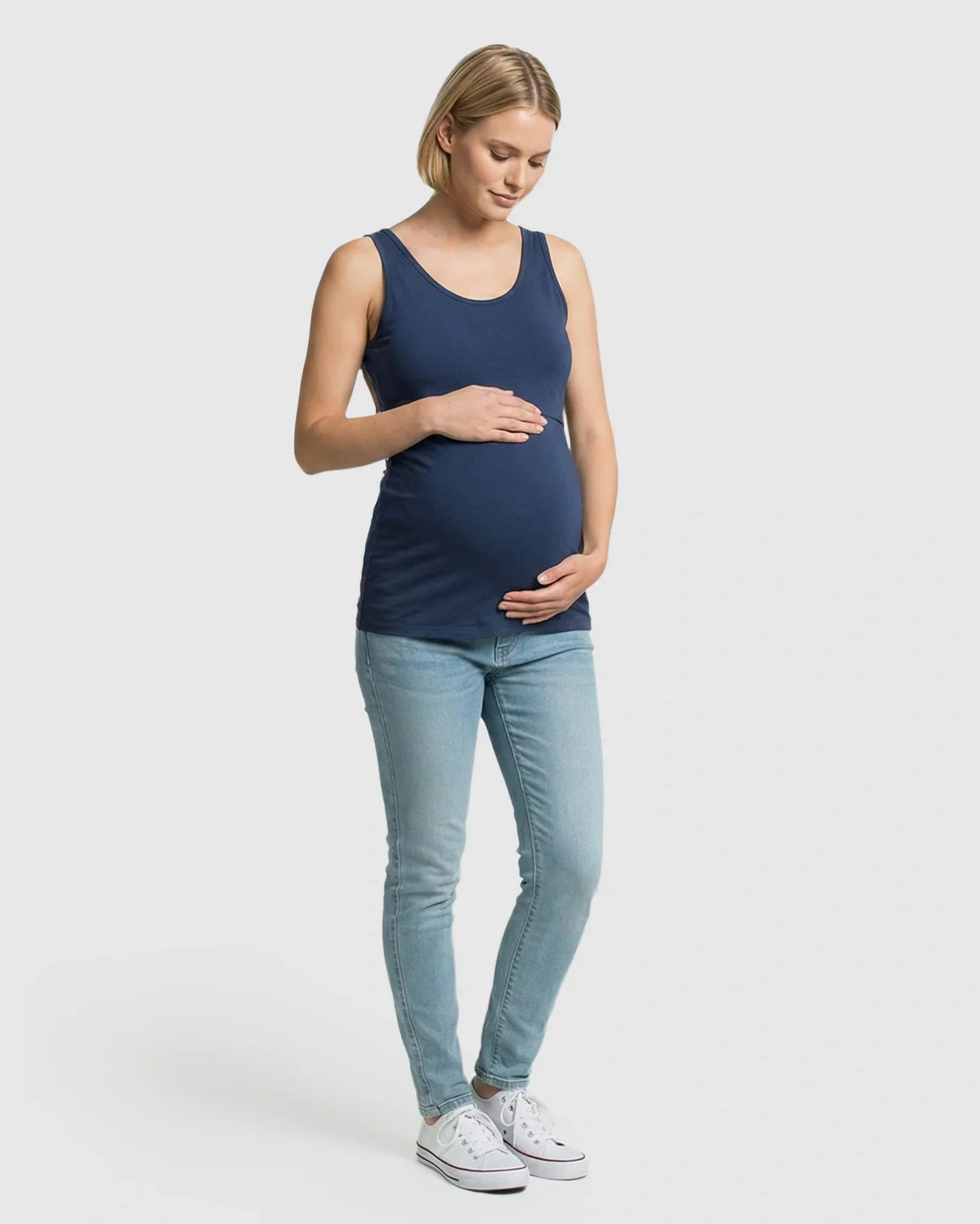 Pregnant woman in a navy blue stretch nursing-access maternity tank top and light wash jeans.