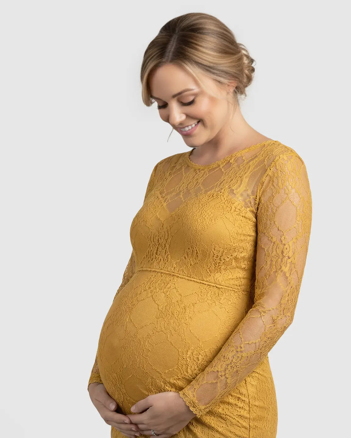Smiling pregnant woman in a mustard sheer lace trumpet maternity photoshoot gown with long sleeves.
