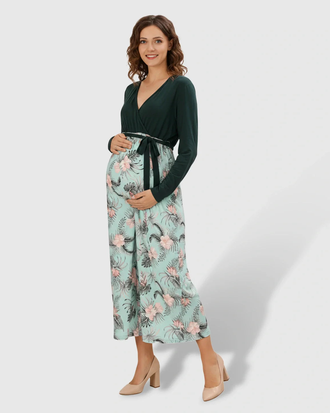 Pregnant woman in a green V-neck long-sleeve maternity midi dress with a floral skirt and tie waist.
