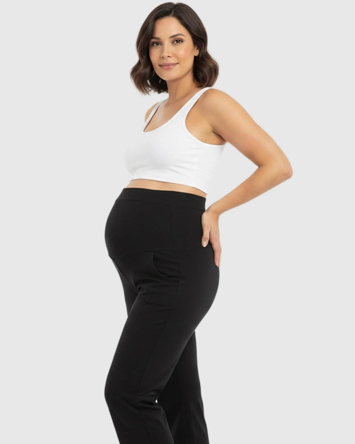 Smiling pregnant woman models black stretch flared maternity pants with an over-belly waistband and pockets.