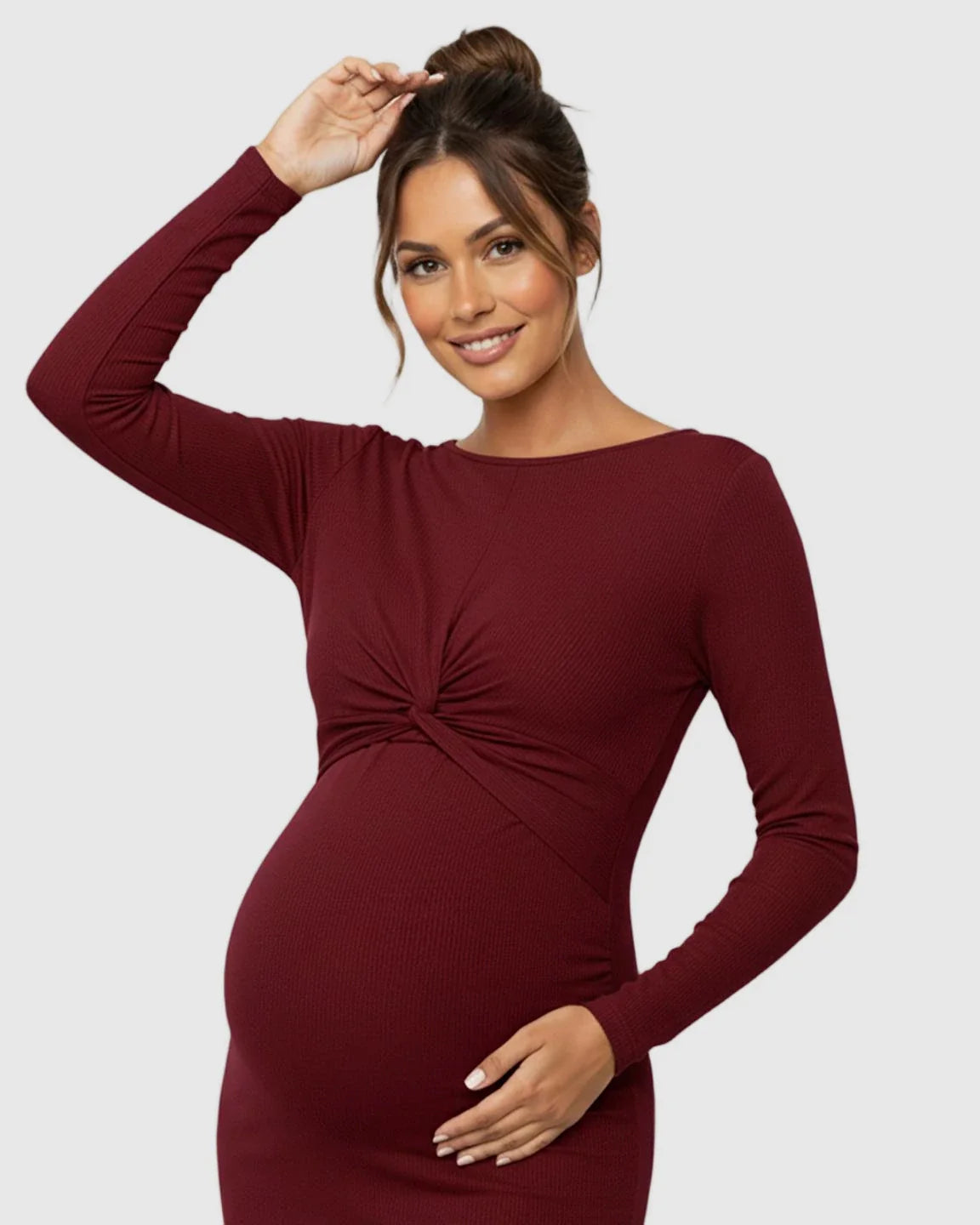 Smiling pregnant woman in a long-sleeve, ribbed, twist-front burgundy bodycon maternity dress.