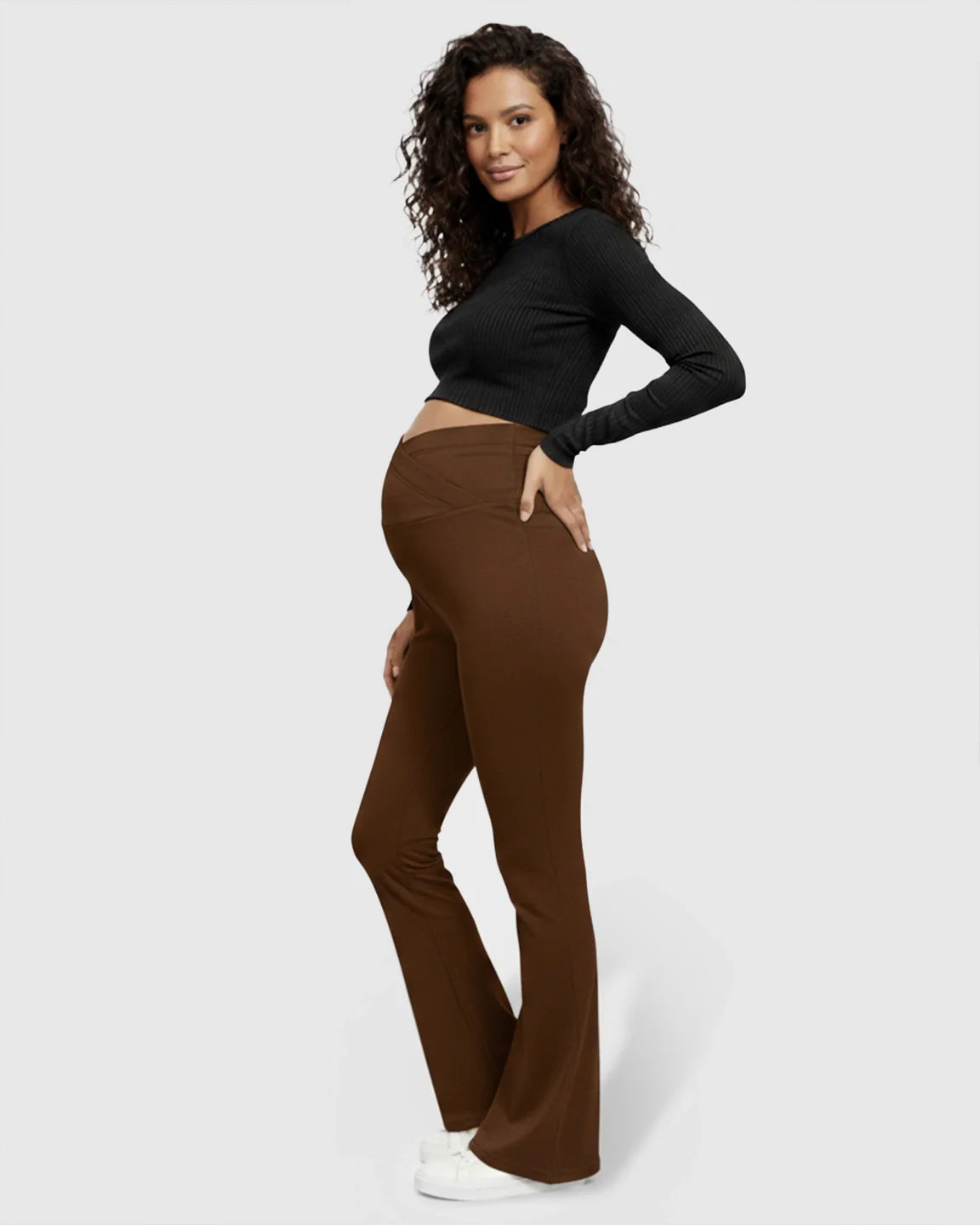 Pregnant woman in brown crossed waistband flared maternity pants and a black crop top.