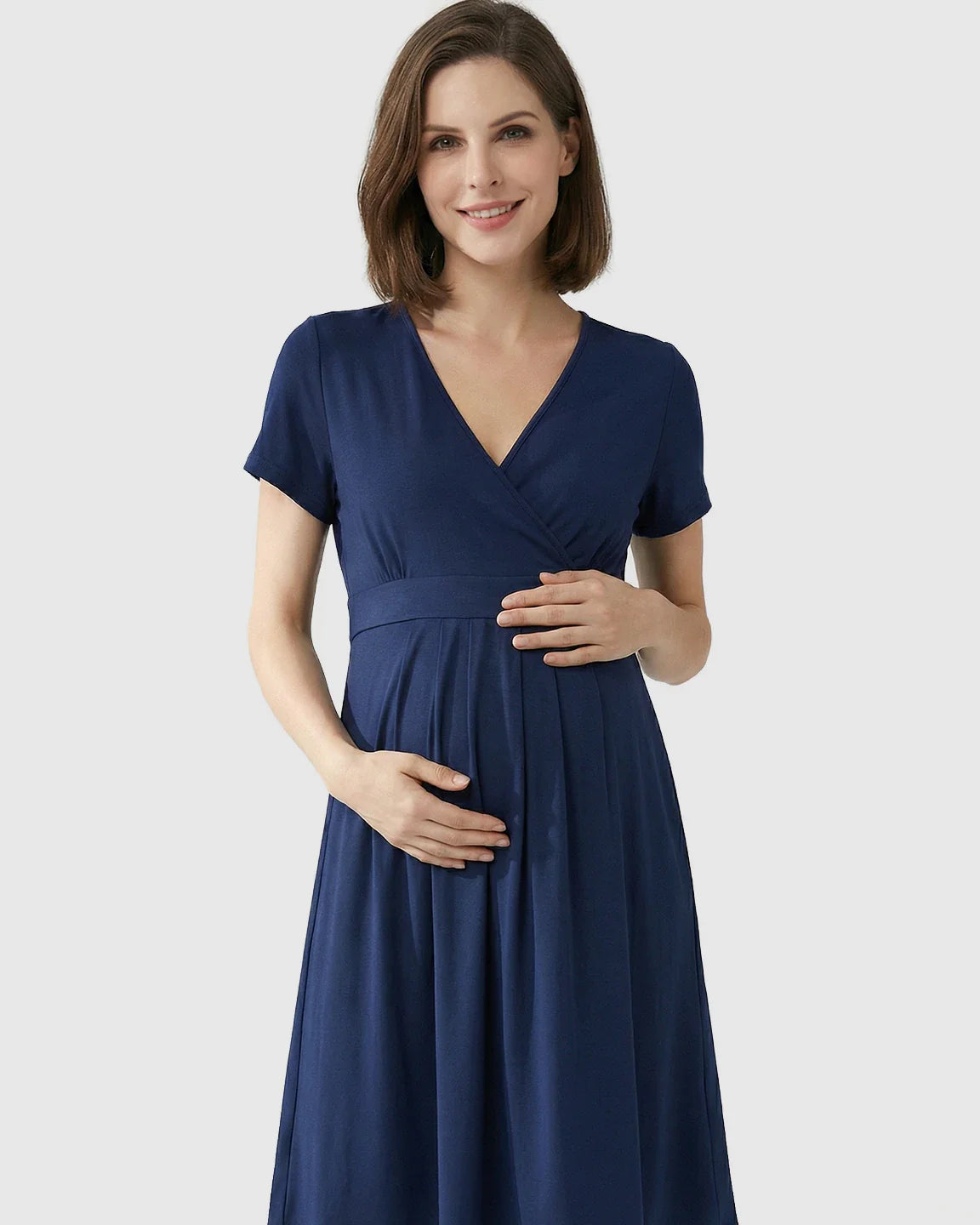 Smiling pregnant woman in a navy V-neck A-line maternity and nursing dress, holding her bump.