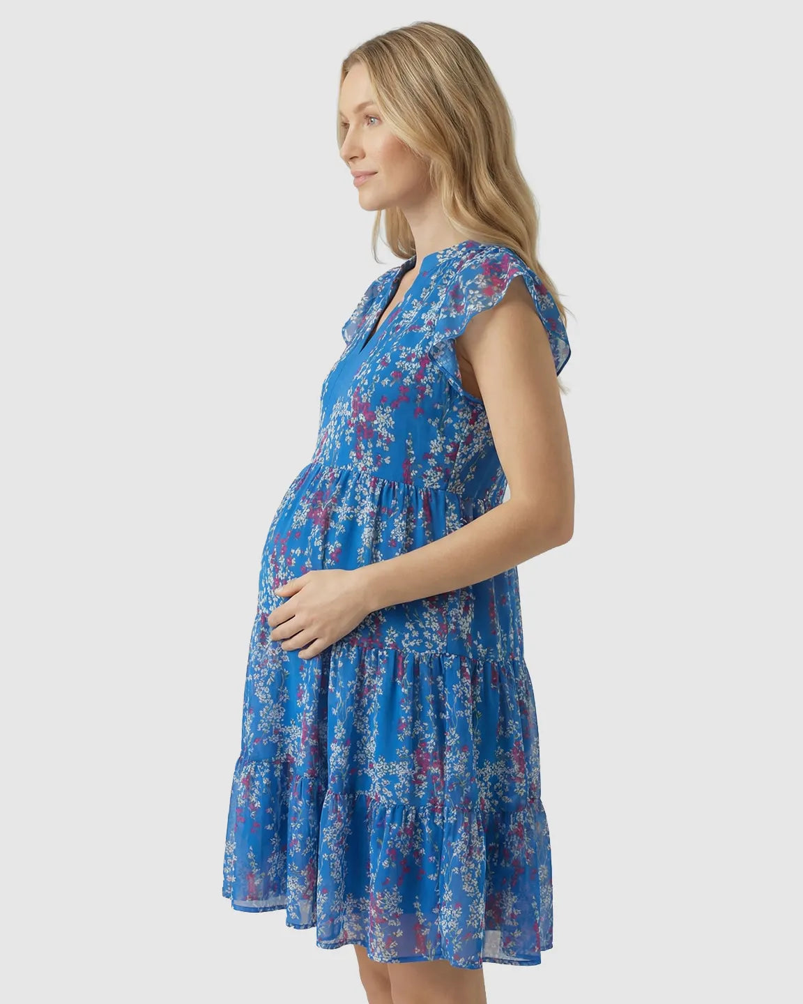Blonde pregnant woman in a blue floral chiffon V-neck A-line maternity dress with tiered ruffles.