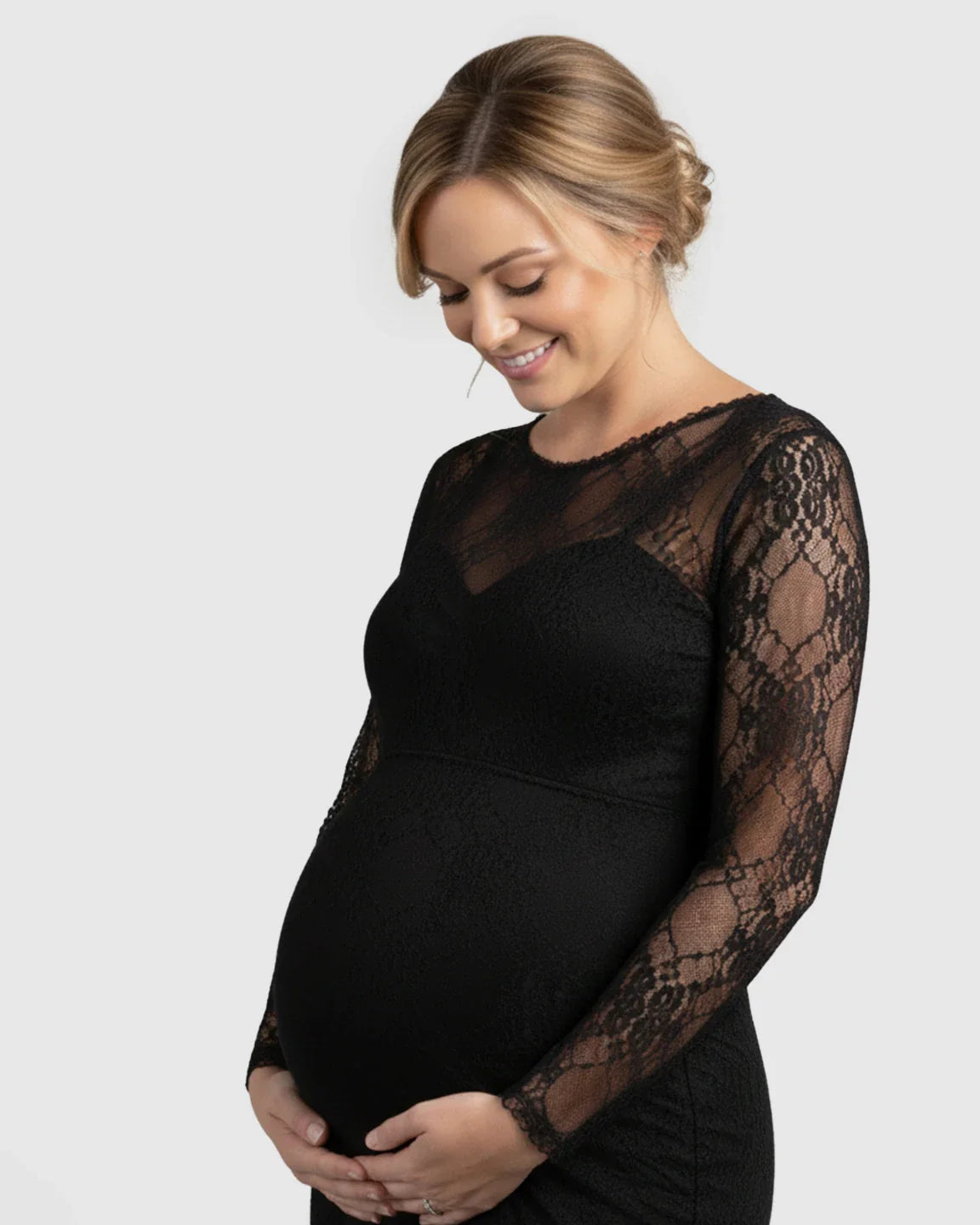 Smiling pregnant woman in a black sheer lace long-sleeve trumpet maternity photoshoot gown.