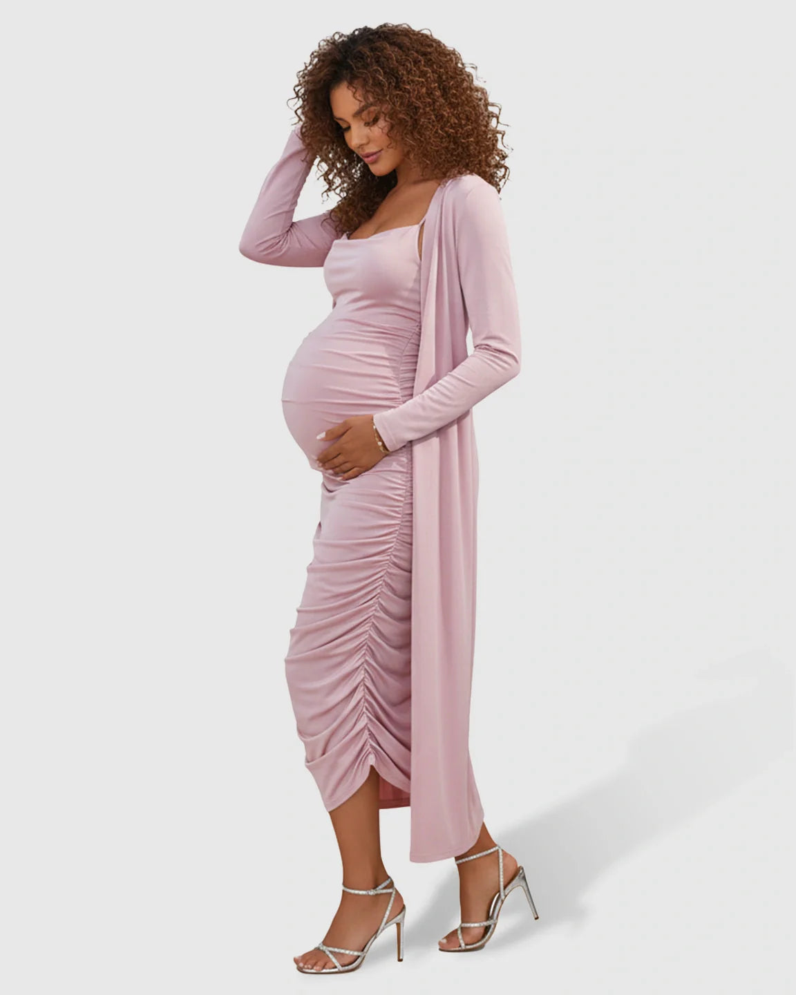 Maternity model in a pink side-ruched slip dress and long-sleeve cardigan with silver heels.