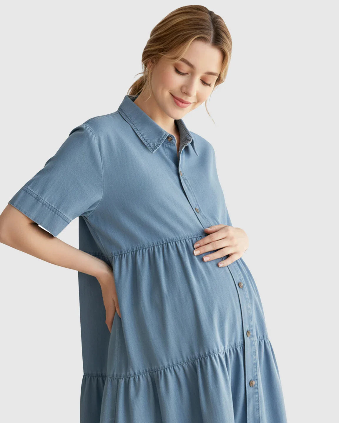 Smiling pregnant woman in a blue tiered denim casual maternity midi dress with button-front.