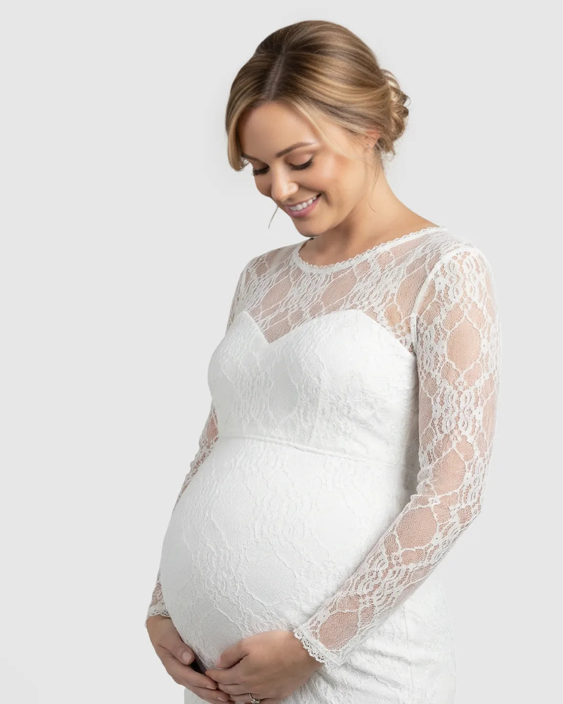 Pregnant woman in a white sheer lace trumpet maternity gown with long sleeves and a classic neckline.