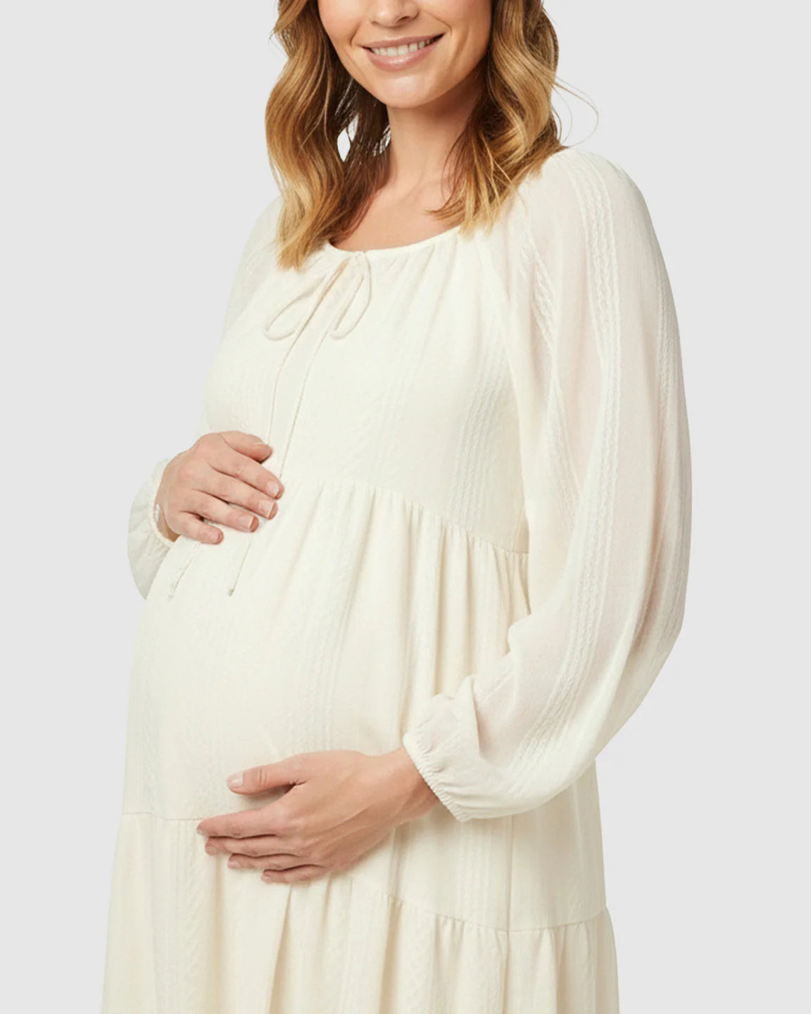Maternity model in a cream tie-front long sleeve tiered midi dress with textured fabric.