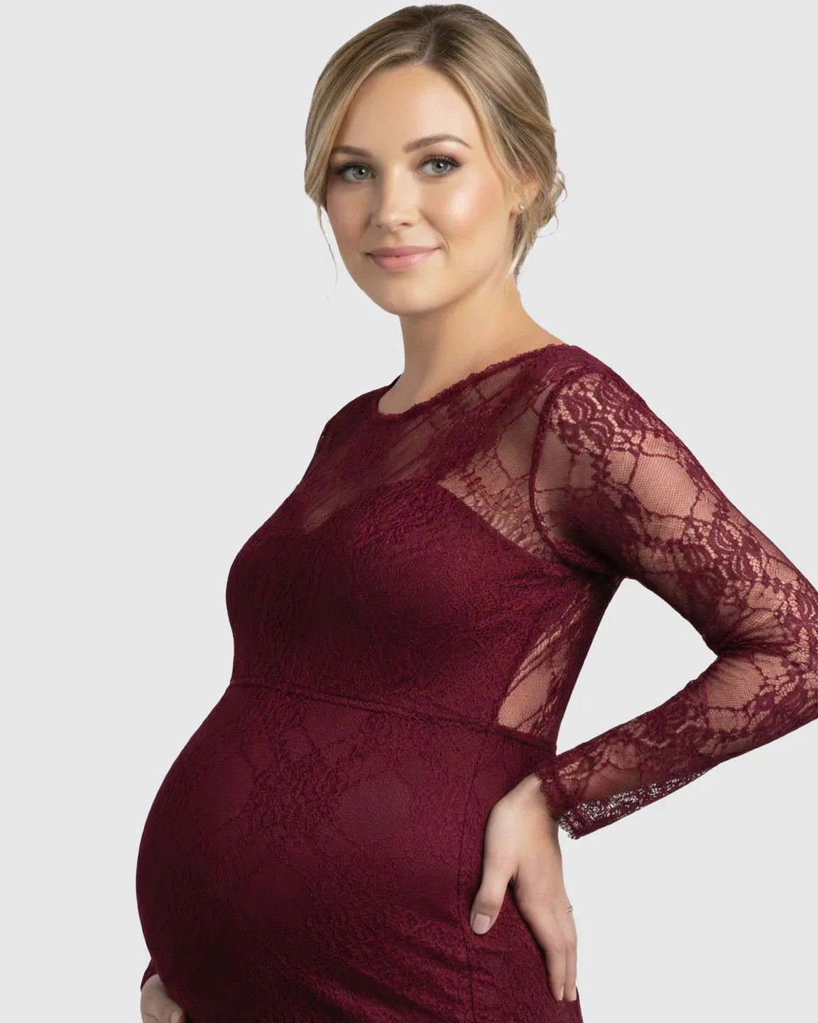 Pregnant woman in a long-sleeved, sheer burgundy lace trumpet maternity gown, highlighting her bump.