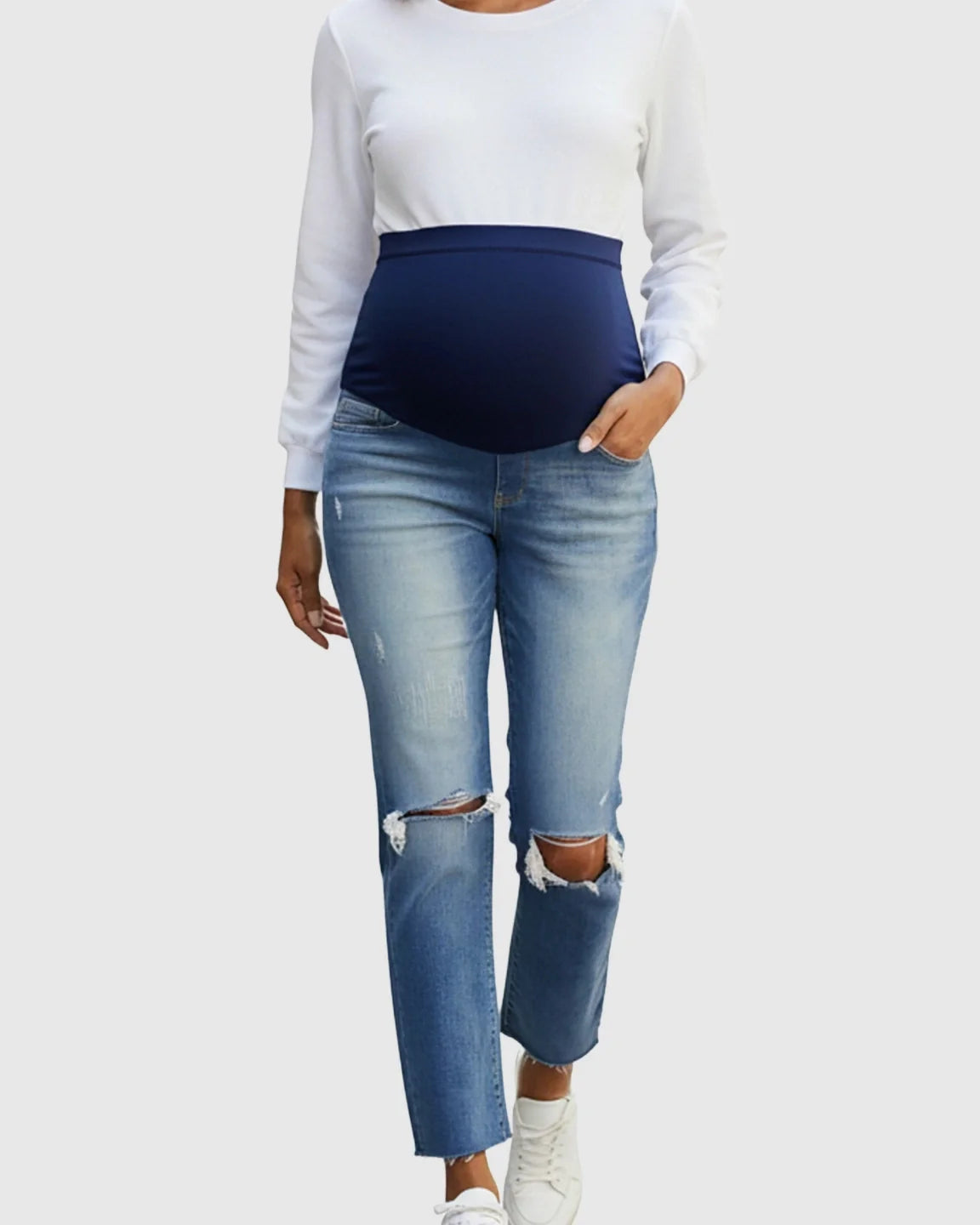 Woman in distressed light wash maternity jeans with a navy belly band and white long-sleeve top.