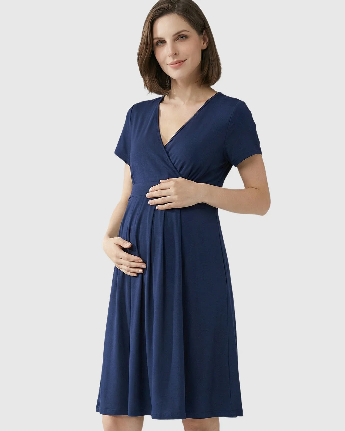 Smiling pregnant woman in a navy V-neck A-line maternity and nursing dress, holding her belly.
