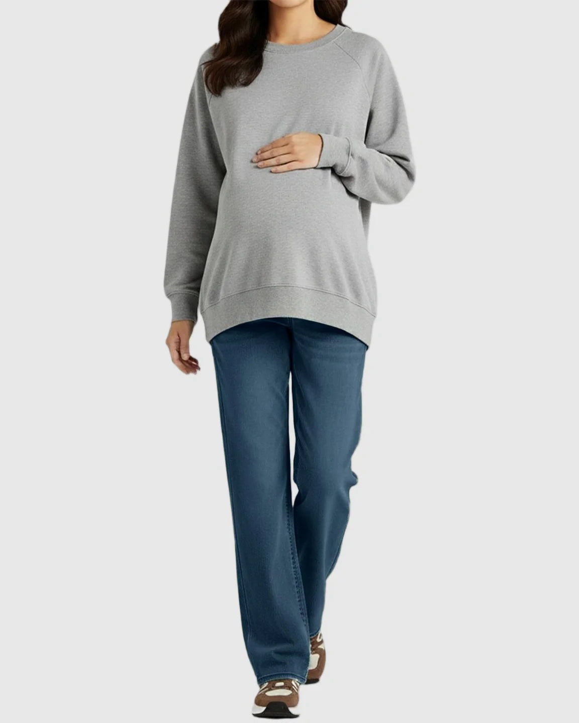Maternity model wearing soft stretch straight-leg blue denim jeans with a grey sweatshirt, cradling her bump.