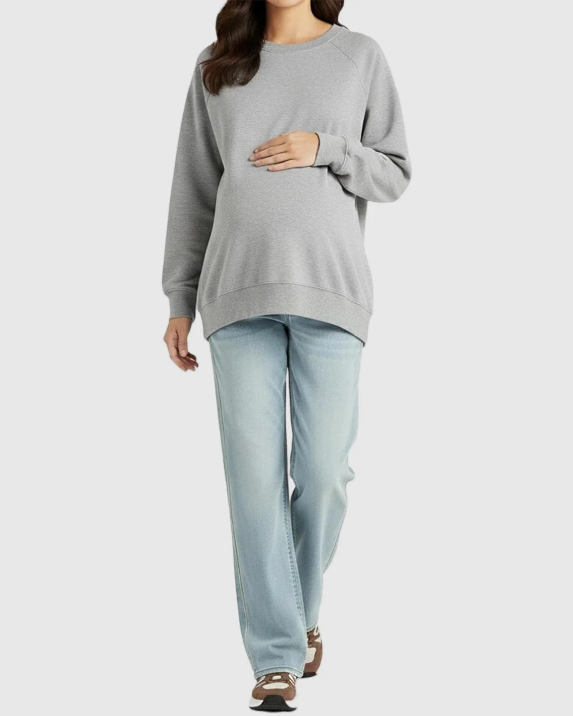 Woman in light blue straight-leg maternity jeans and a gray sweatshirt, cradling her baby bump.