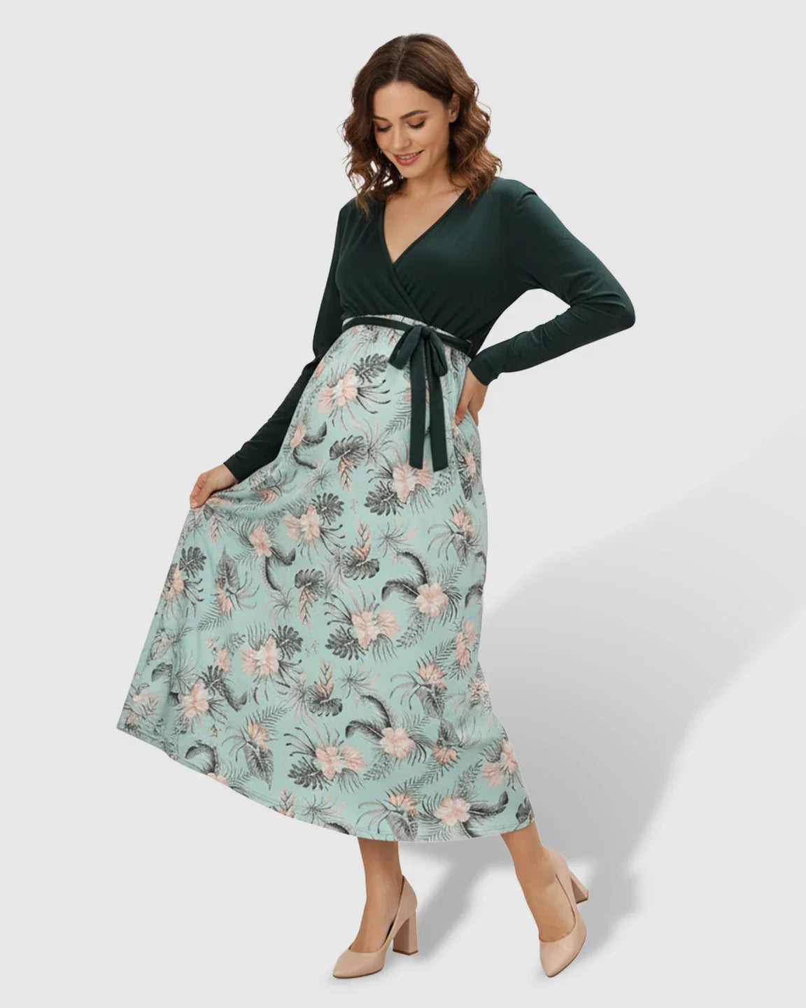 Woman in a long-sleeve V-neck deep green and floral print maternity midi dress with a tie waist.