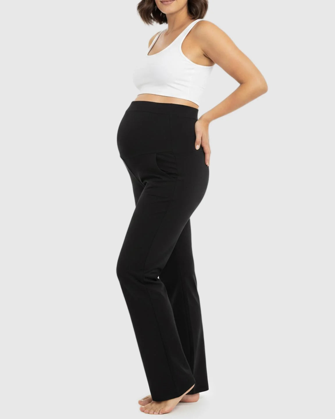 Pregnant woman in black stretch flared maternity pants with an over-belly waistband and pockets.