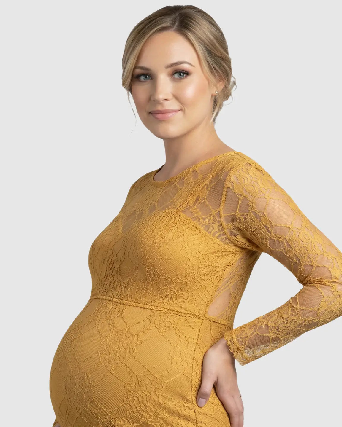 Pregnant woman in a mustard yellow sheer lace long-sleeve trumpet maternity gown.