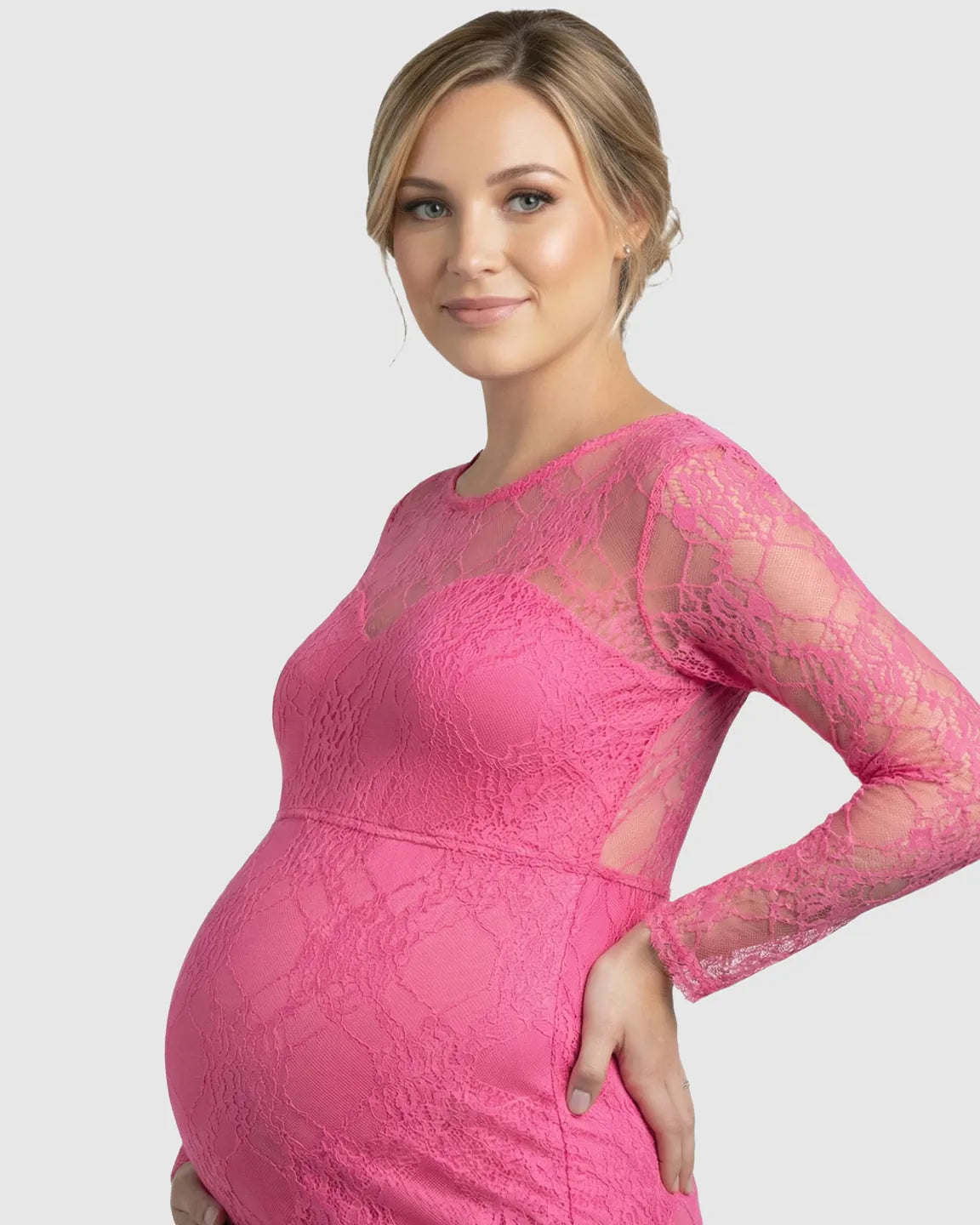 Pregnant woman in a pink sheer lace trumpet maternity gown with long sleeves, classic neckline, and mermaid skirt.