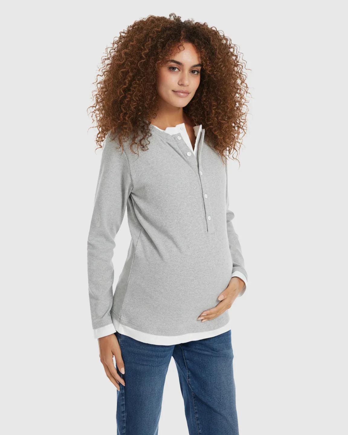 Woman in a gray long-sleeve button-front henley maternity and nursing top with a white undershirt, holding her pregnant belly.