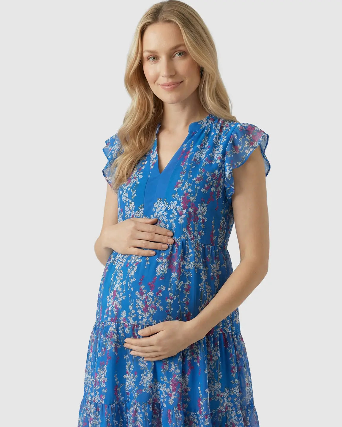Blonde pregnant woman in a blue floral chiffon V-neck A-line maternity dress with ruffled cap sleeves.