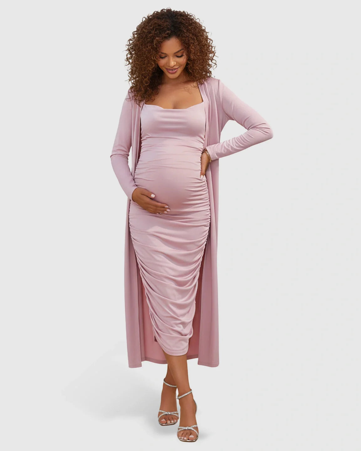 Pregnant woman in a pink side-ruched slip dress and long-sleeve cardigan maternity set.