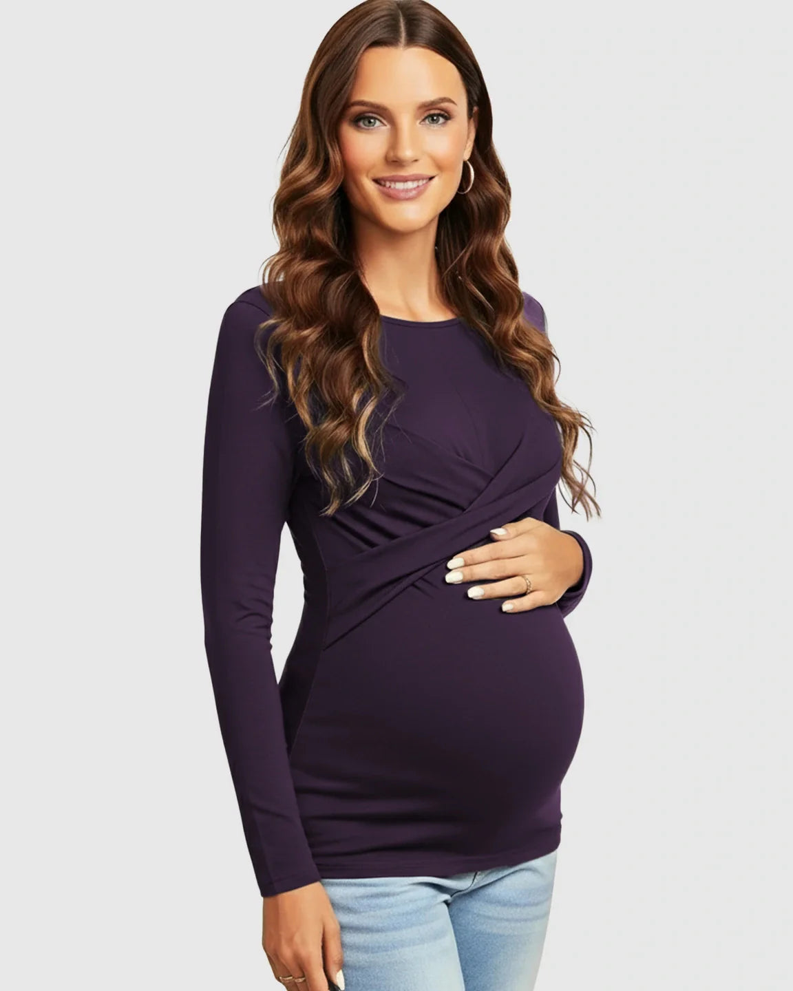 Smiling pregnant woman in a purple cross-pleat fitted long sleeve maternity top and jeans.