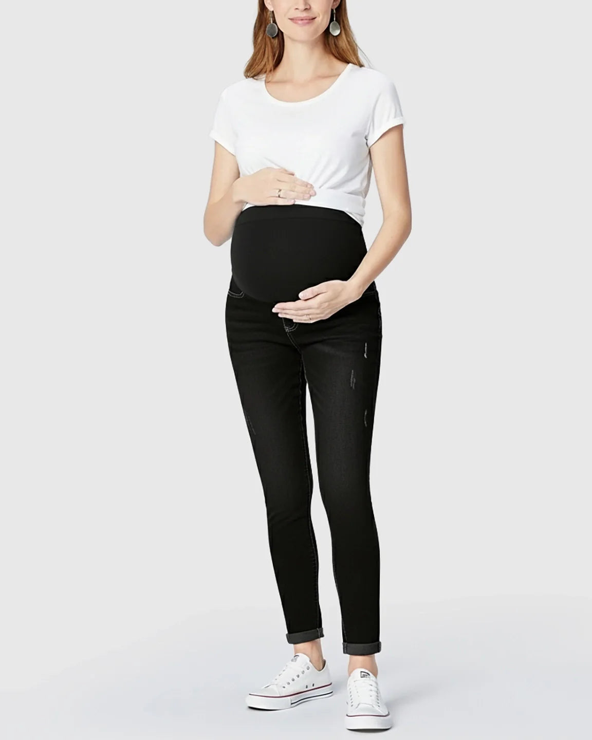 Maternity model in black distressed skinny jeans with full panel, white tee, and sneakers.