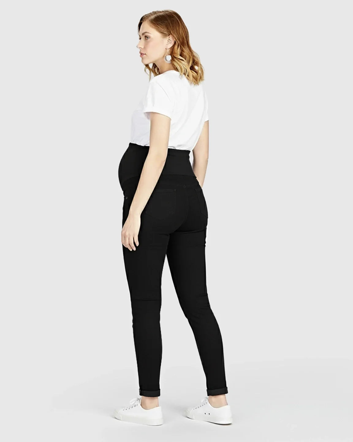 Pregnant woman in black full panel maternity skinny jeans with a white t-shirt and sneakers.