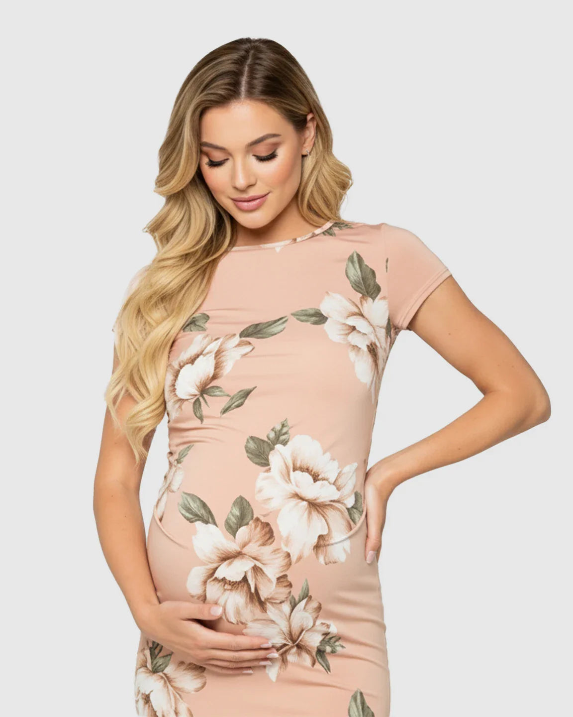 Blonde pregnant woman in a peach stretchy floral fitted maternity midi dress, hands on bump.
