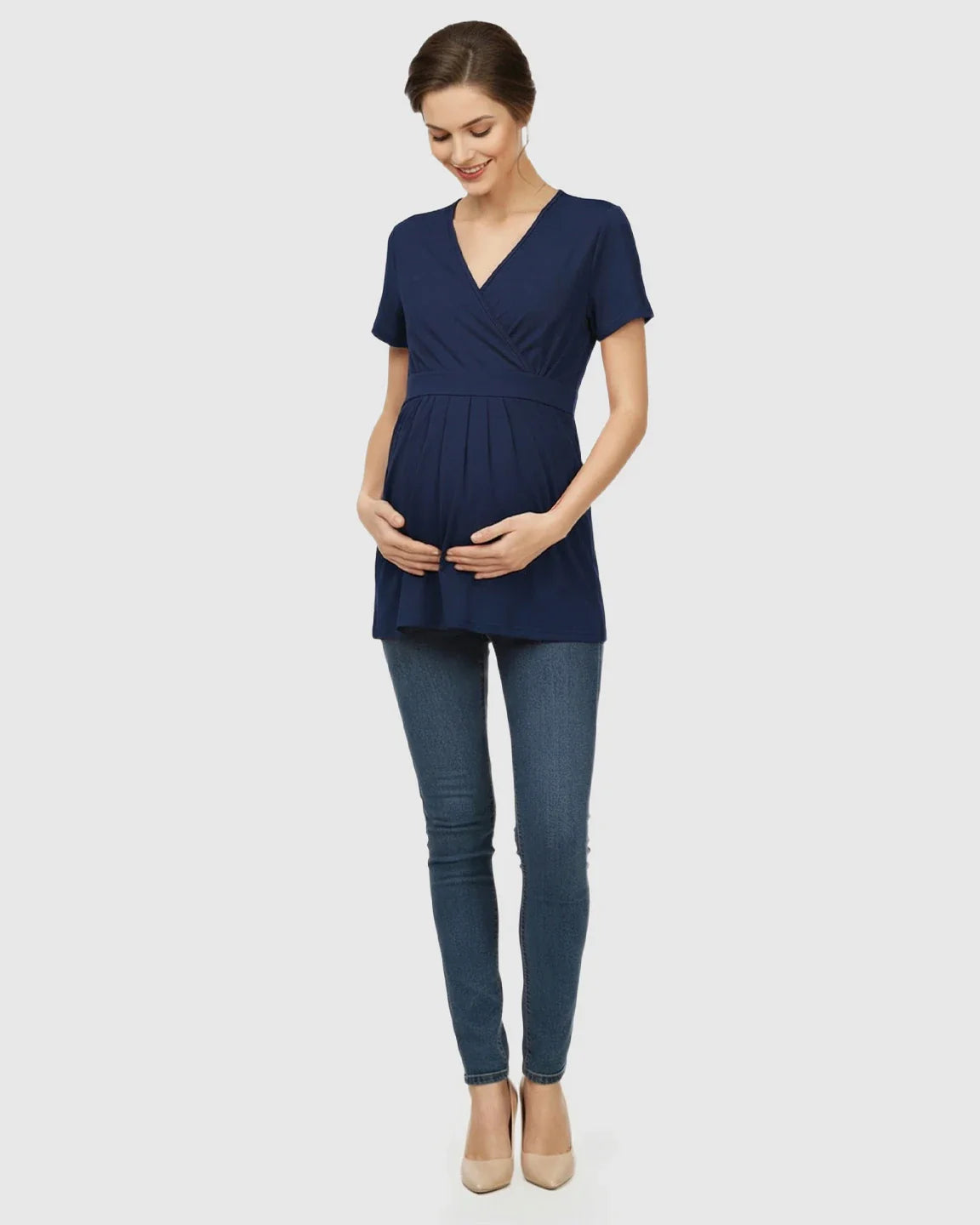 Smiling pregnant woman in a navy V-neck wrap-style maternity top with short sleeves and an adjustable waist tie.