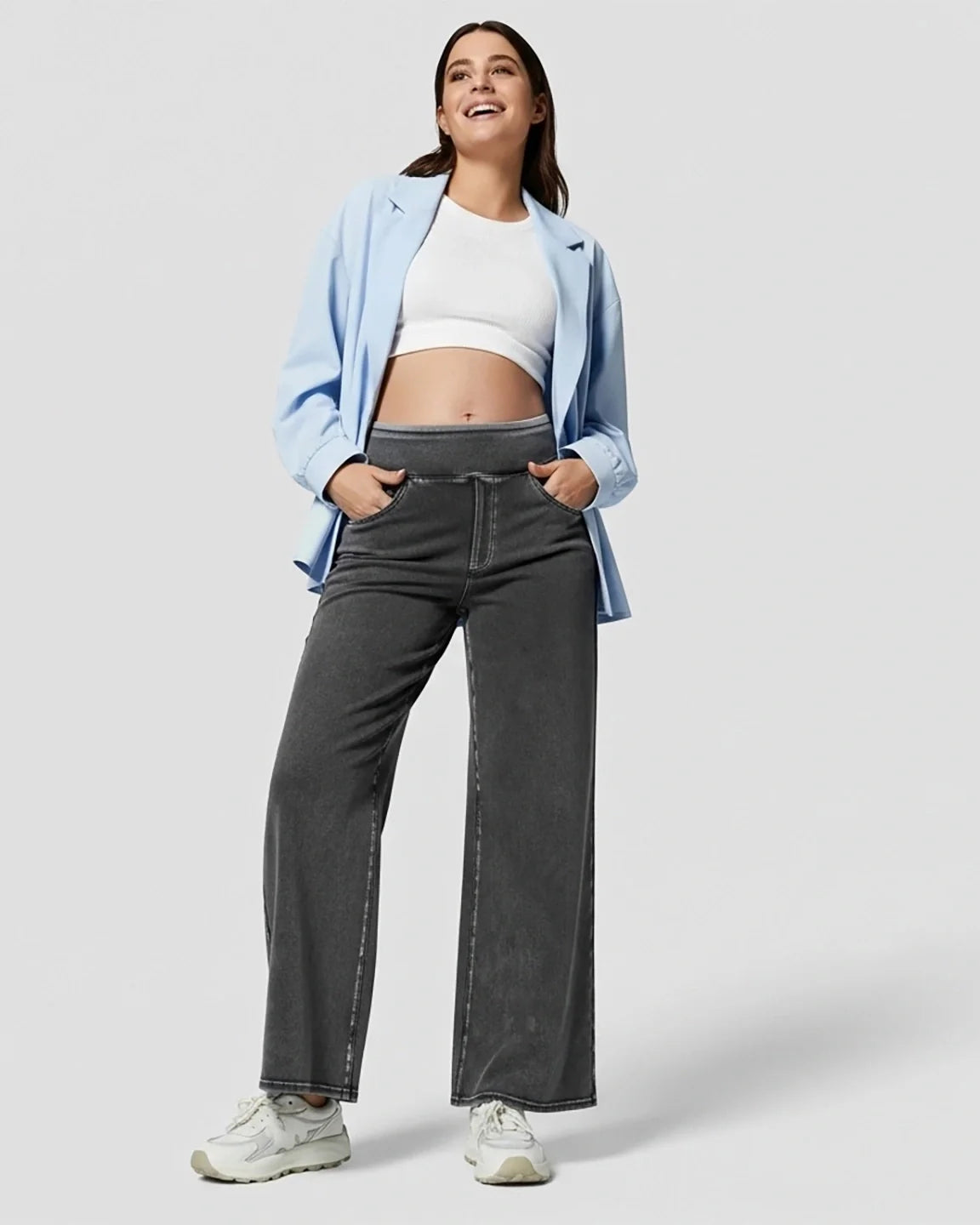 Smiling pregnant woman in charcoal high-waist wide-leg maternity denim jeans, white crop top, and blue blazer.