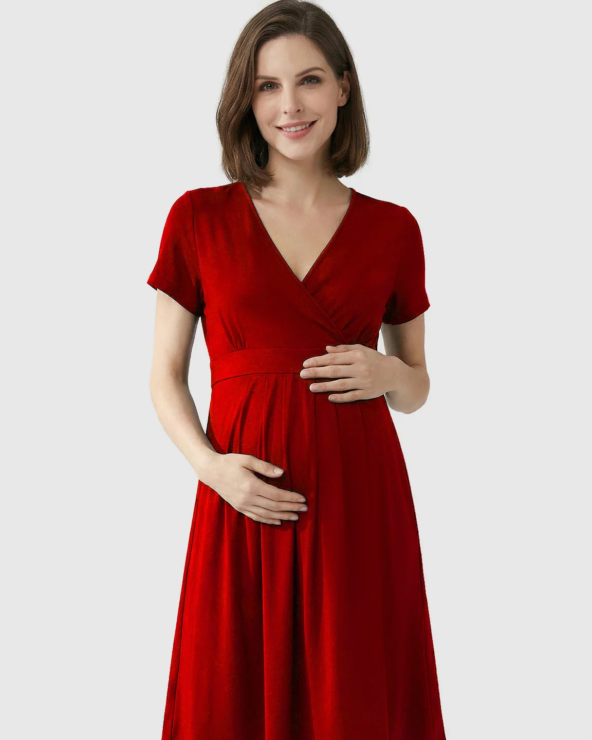 Smiling pregnant woman in a red V-neck A-line maternity and nursing dress, holding her bump.